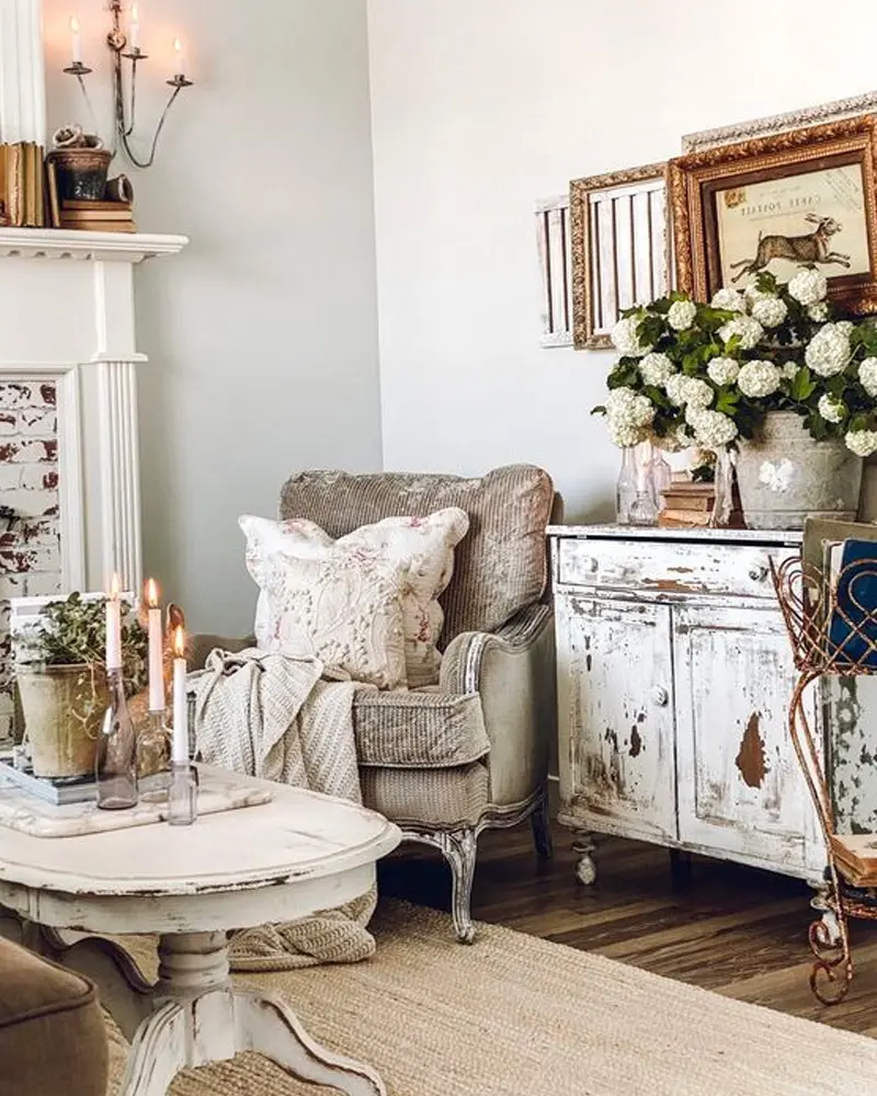 Chippy white painted cabinet, a gray upholstered armchair and white hydrangeas