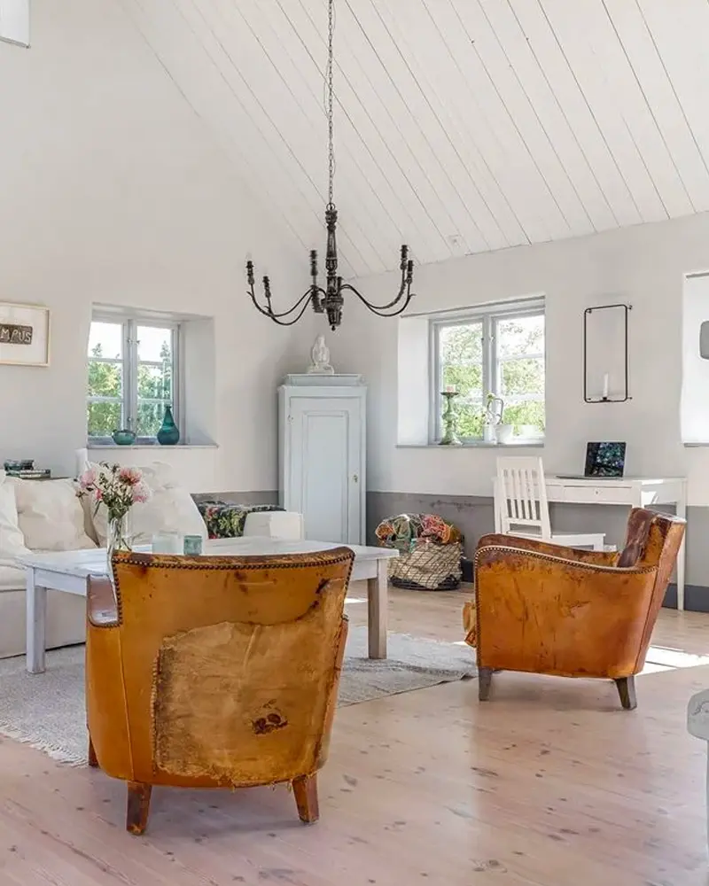 Two worn cognac leather armchairs, a wrought-iron chandelier and a white painted cupboard
