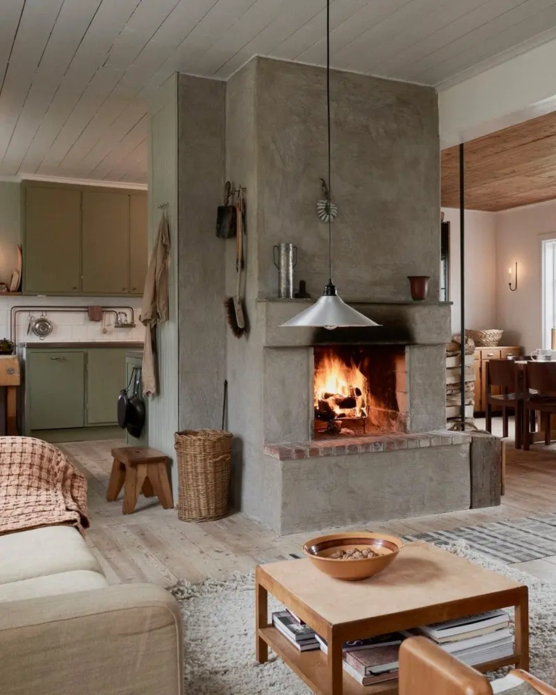 Freestanding concrete fireplace with a crackling fire, a wood coffee table and a basket of logs