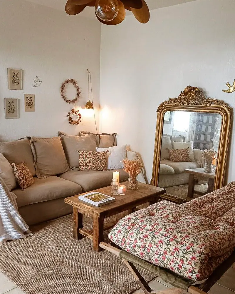 Taupe sofa, a gilded floor mirror and a floral floor cushion on a woven rug