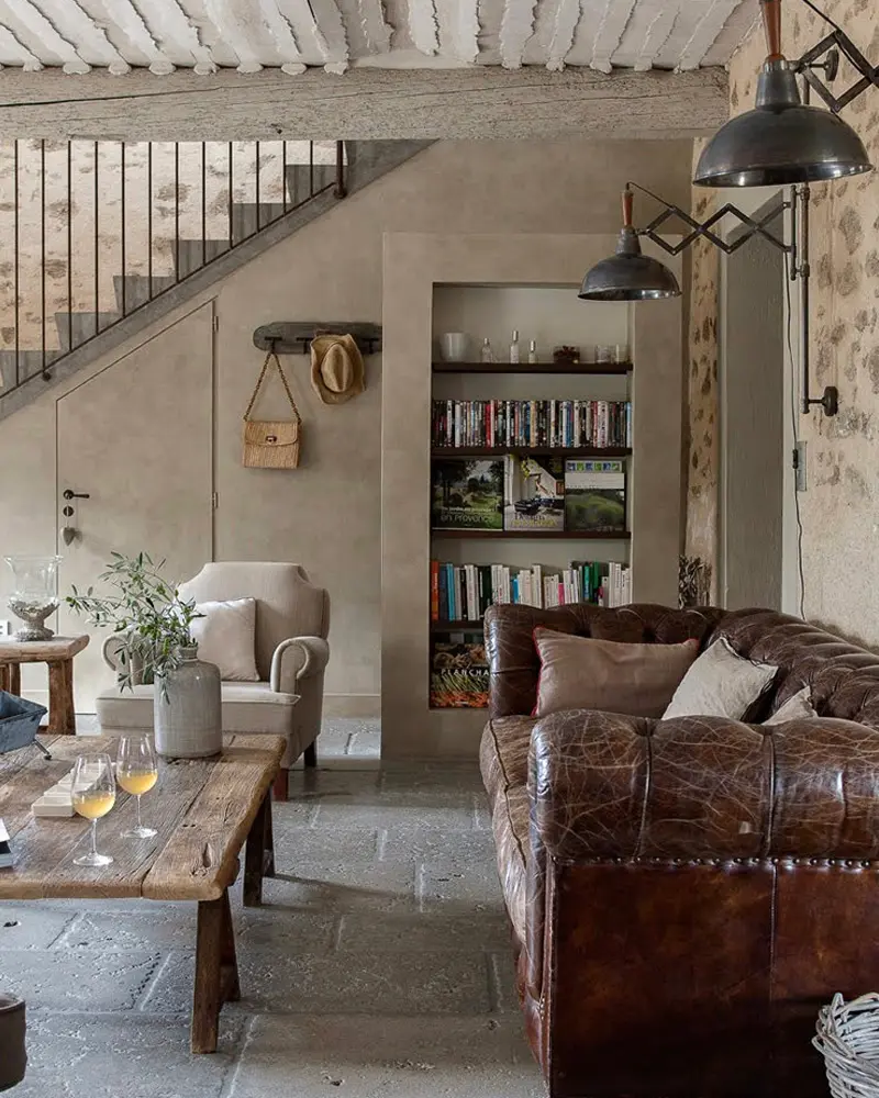 Brown leather Chesterfield sofa, a rustic wood coffee table and built-in bookshelves under a beamed ceiling
