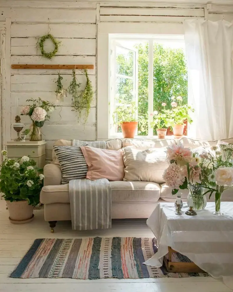 Pink sofa, rag rug, potted plants and wreaths on white paneling