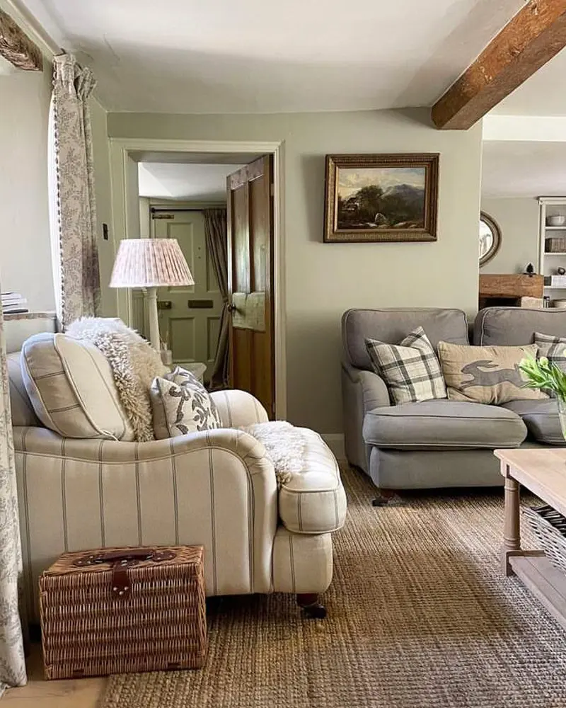 Sage green walls, a striped armchair, a gray loveseat and a landscape painting