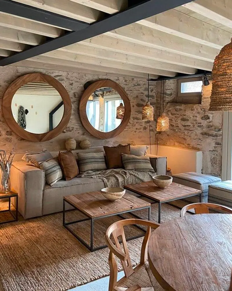 Exposed stone wall with two round wood mirrors above a gray sofa and wood coffee tables