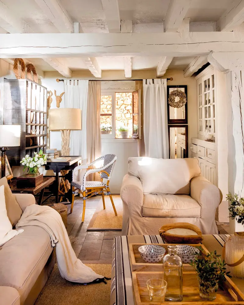 White-painted beams, cream armchairs and a tray-topped ottoman in a cozy cottage living room