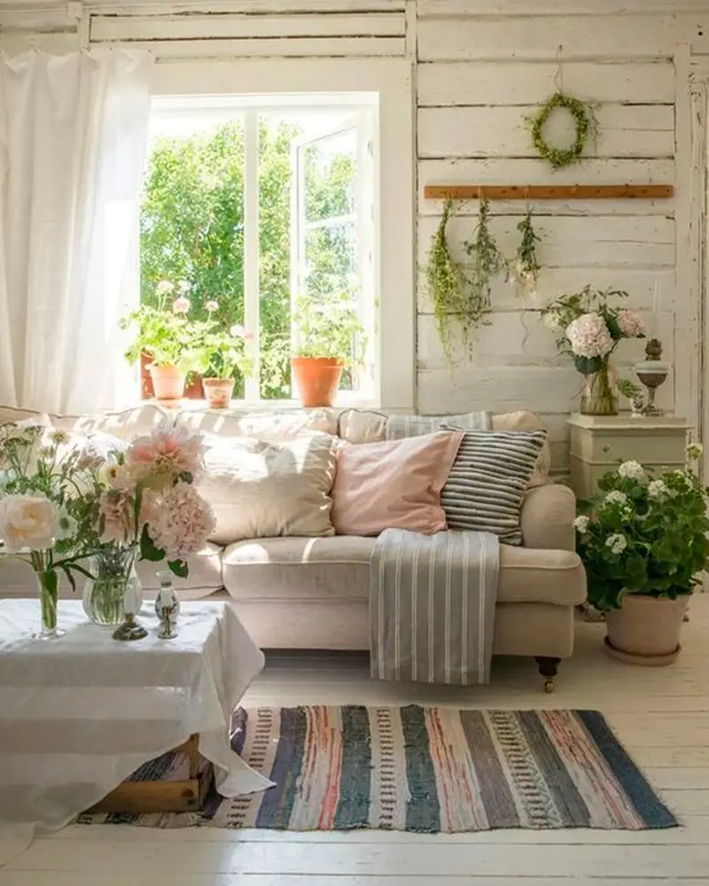 Whitewashed plank walls, a pink-pillowed sofa, garden flowers and a striped rug