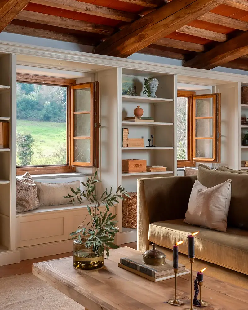 Dark wood ceiling beams, built-in shelves around a window seat and an olive-green sofa