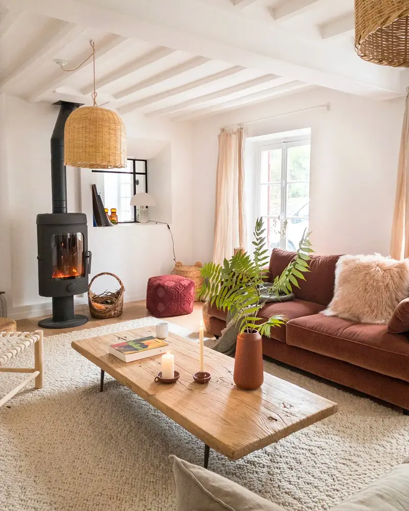 Black wood stove, a rust velvet sofa and a plank coffee table under white beams