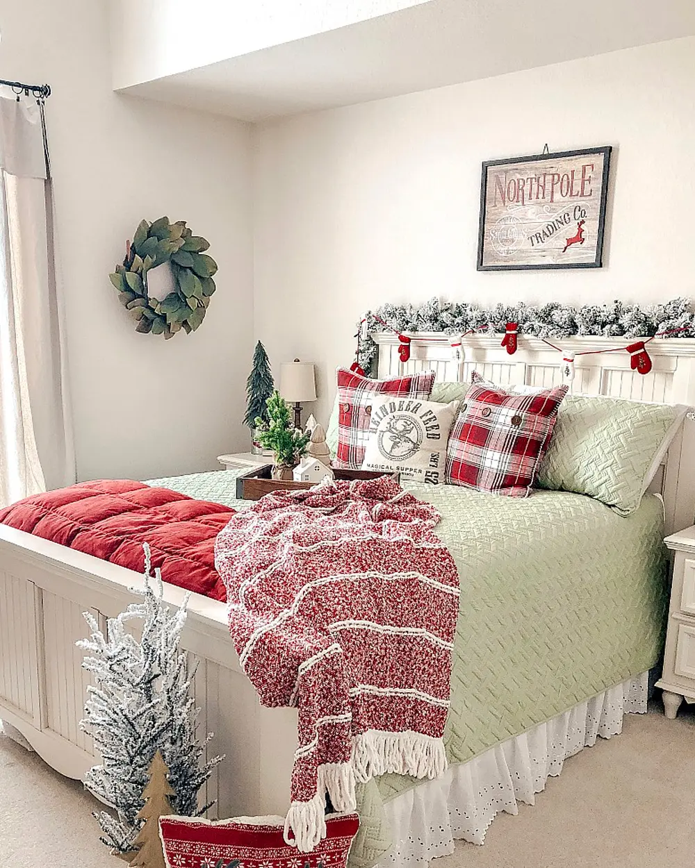 Farmhouse bedroom with green quilt, red plaid pillows, a red knit throw and a North Pole sign