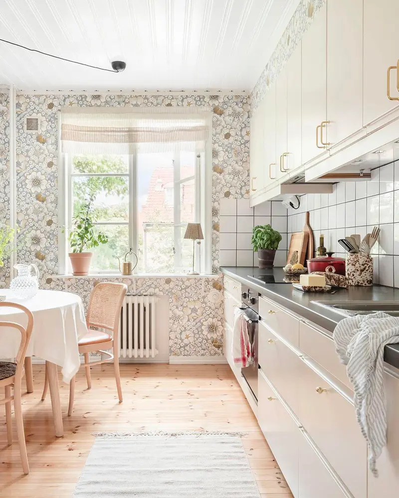 Galley kitchen with floral wallpaper, white cabinets, round table and bentwood chairs
