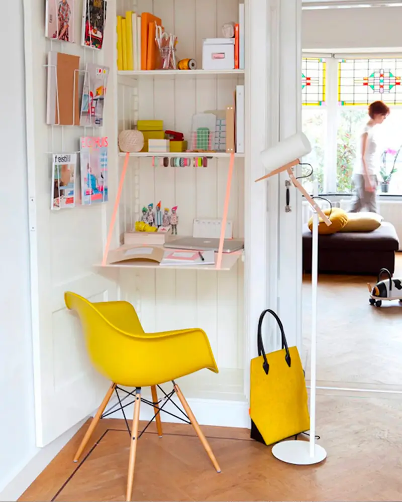 Wall-mounted drop-down desk with yellow chair and shelf above