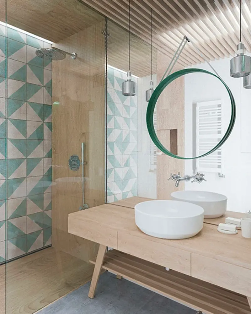 Light wood vanity with two round basins, green round mirror and teal triangle tiles in the shower