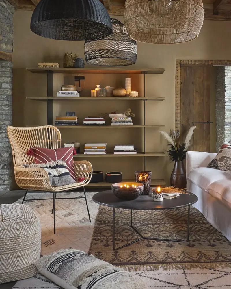 Rattan armchair with patterned pillow, metal shelving, black woven pendants and layered rugs