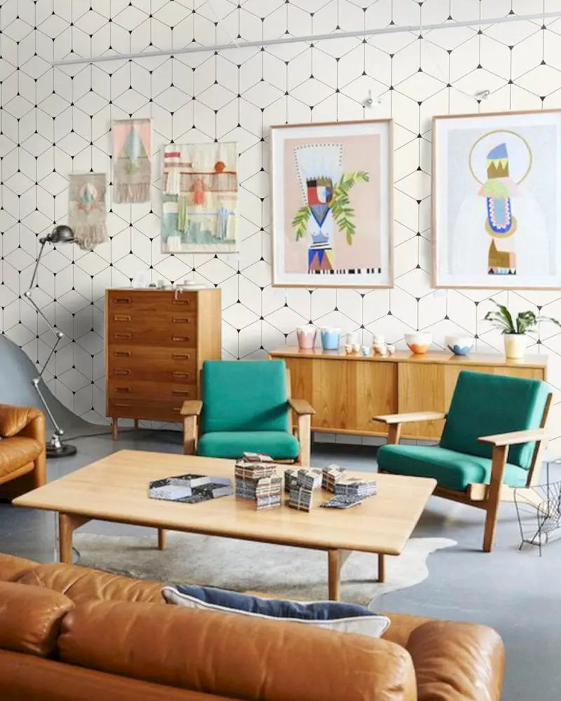 Green armchairs, cognac leather sofa and teak cabinets against patterned wallpaper