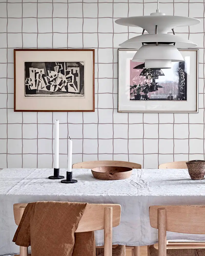 Grid-pattern wallpaper with framed prints, white pendant, linen tablecloth and black candlesticks