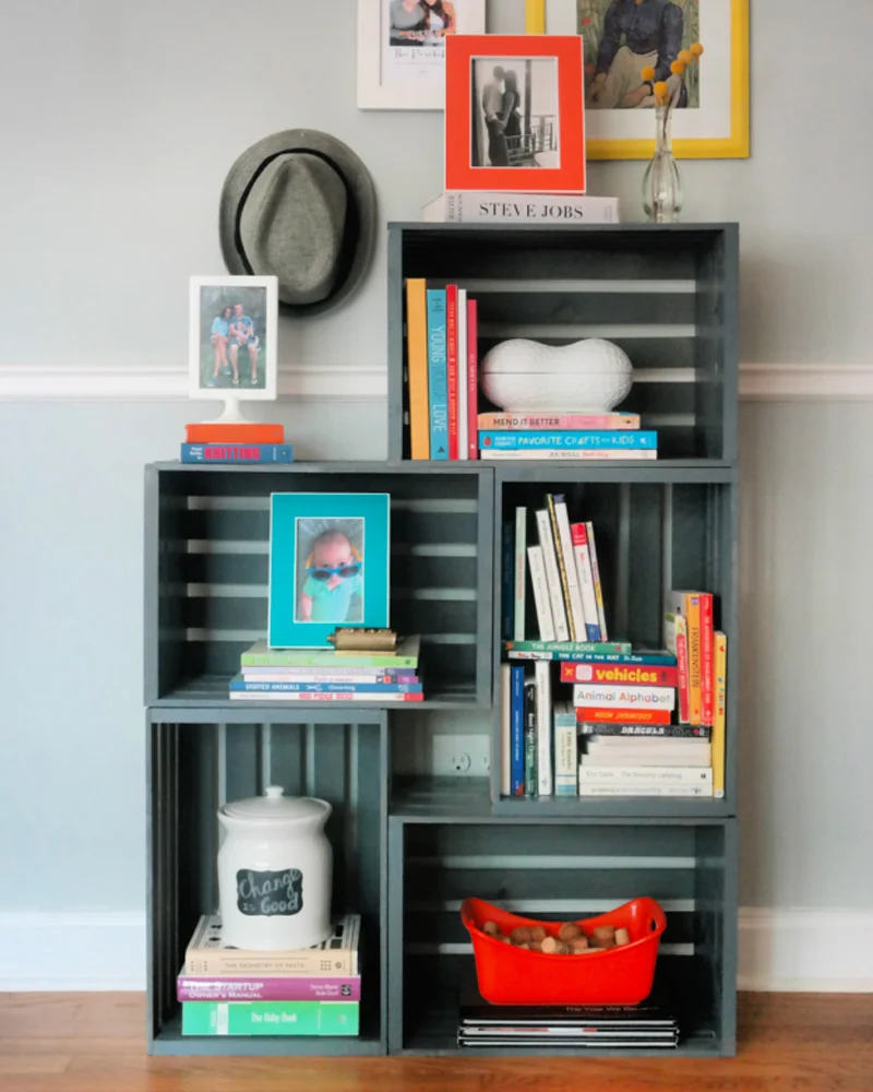 Bookshelf of crates painted dark gray-green holding books and frames