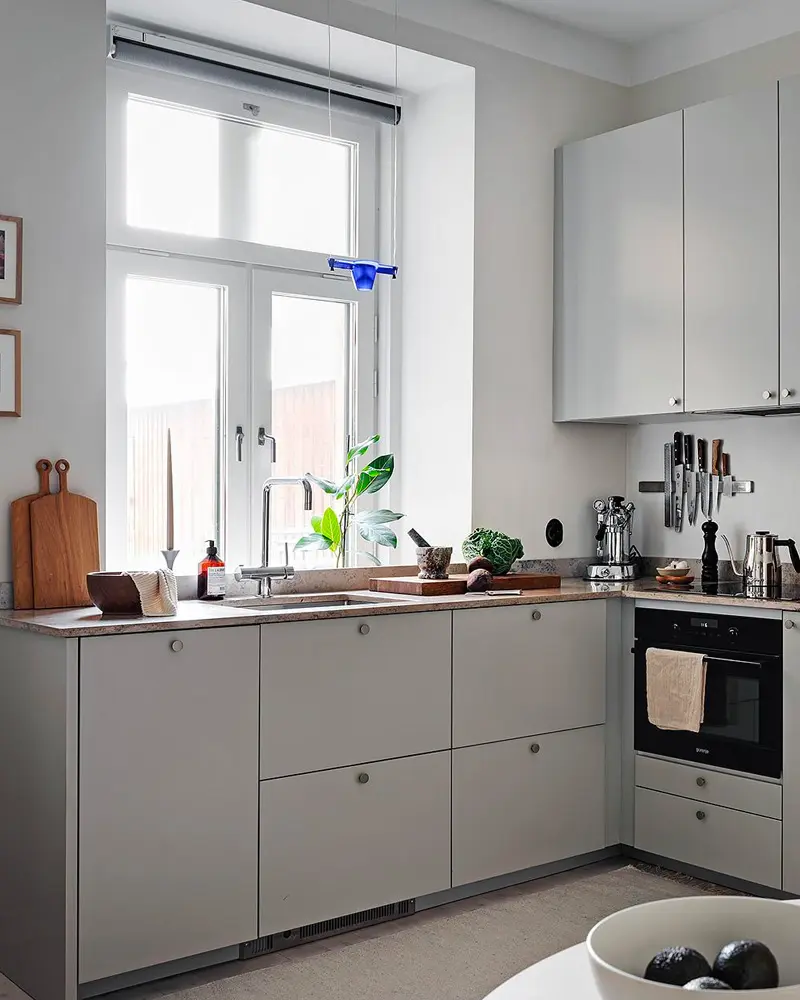 Light gray L-shaped kitchen with drawer fronts, wood cutting board and black oven