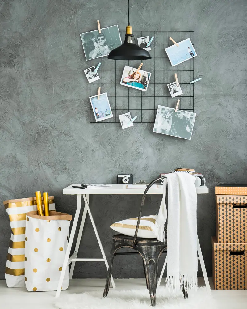 Concrete-look wall with black wire grid memo board, white desk, black metal chair and kraft storage boxes