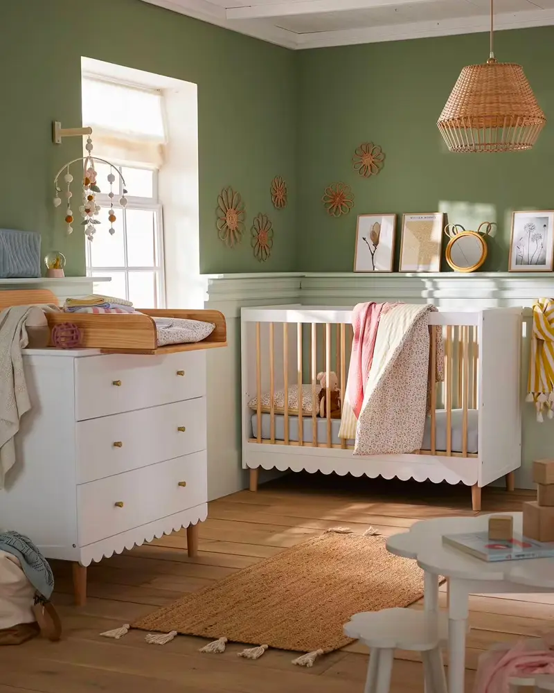 Olive green nursery with scalloped white dresser and crib, rattan pendant and woven sunburst mirrors
