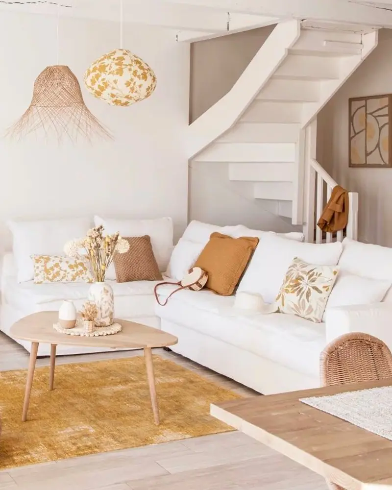 White sofa with ochre pillows, round wood table, yellow rug and two woven pendants by a staircase