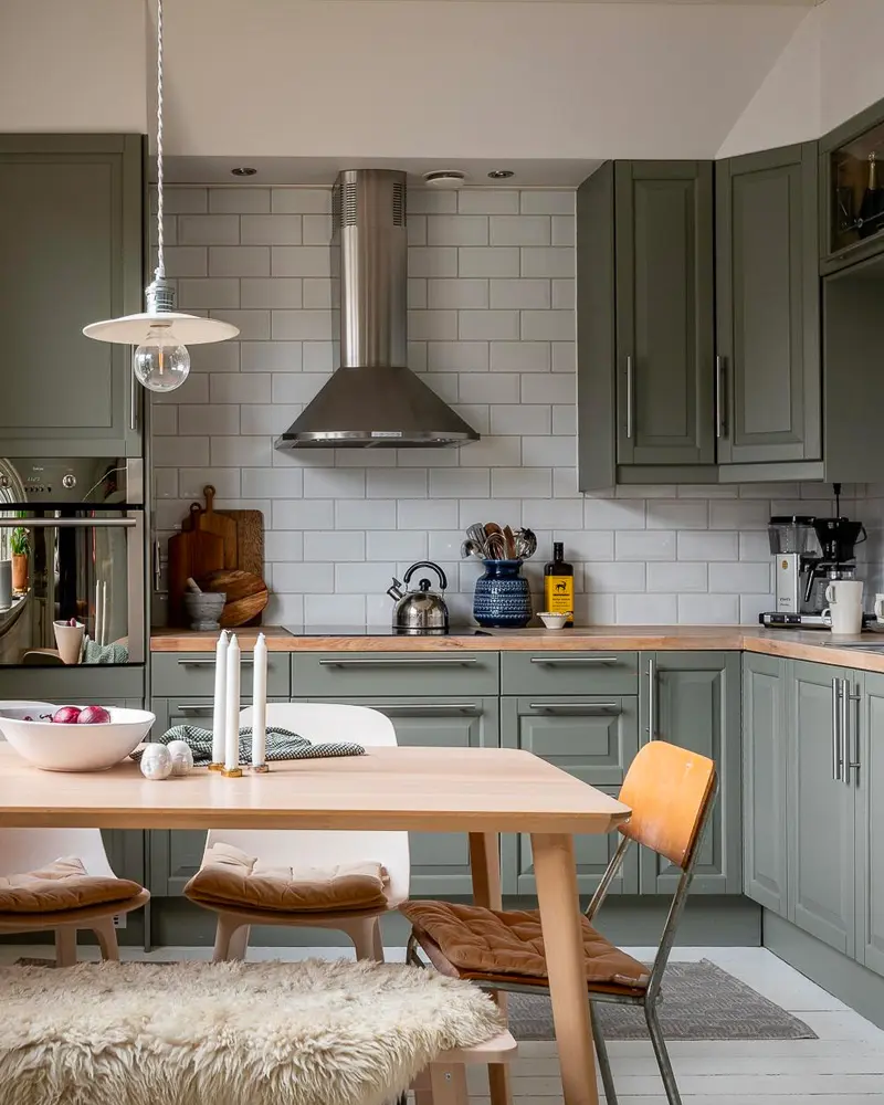 Sage green cabinets with subway tile, stainless hood, wood table and sheepskin on a chair