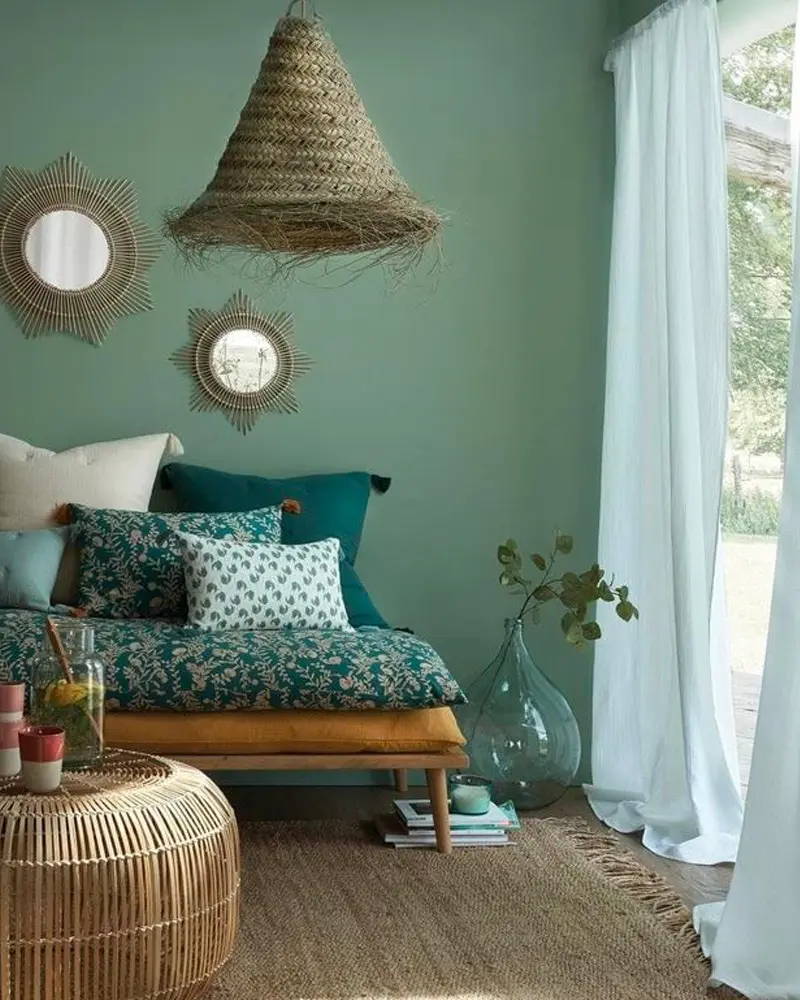 Sage green wall with rattan mirrors, daybed with floral pillows, woven pendant and glass vase