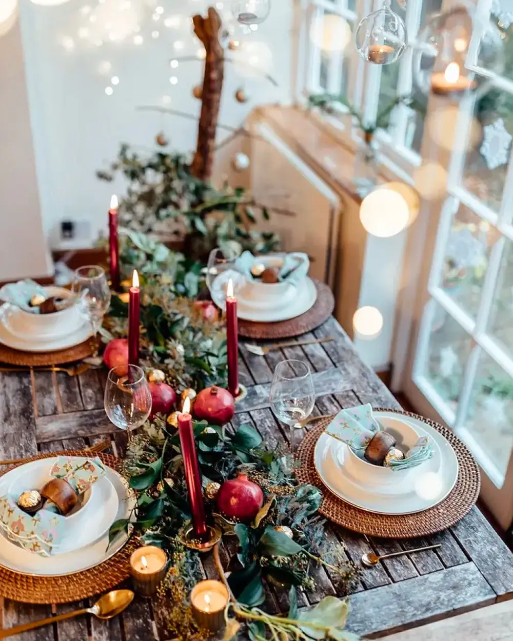 Weathered wood table with a greenery garland, red tapers, pomegranates and rattan chargers