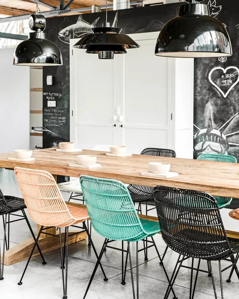 Long wood table with black, turquoise and natural wicker chairs under black dome pendants