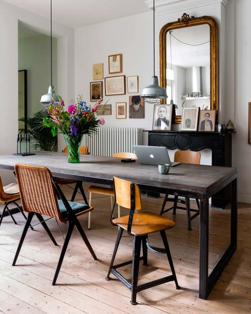 Gray dining table with metal legs, mixed chairs and a gilded mirror over a fireplace