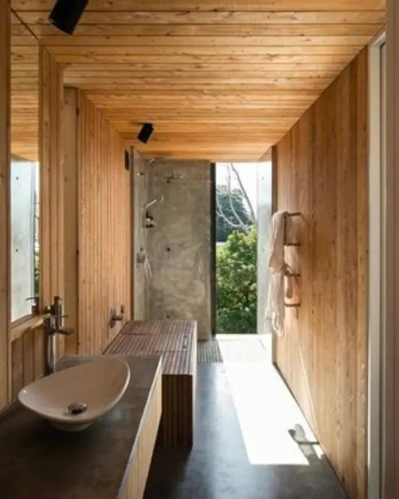 Narrow bathroom lined with wood planks, a vessel sink and an open shower