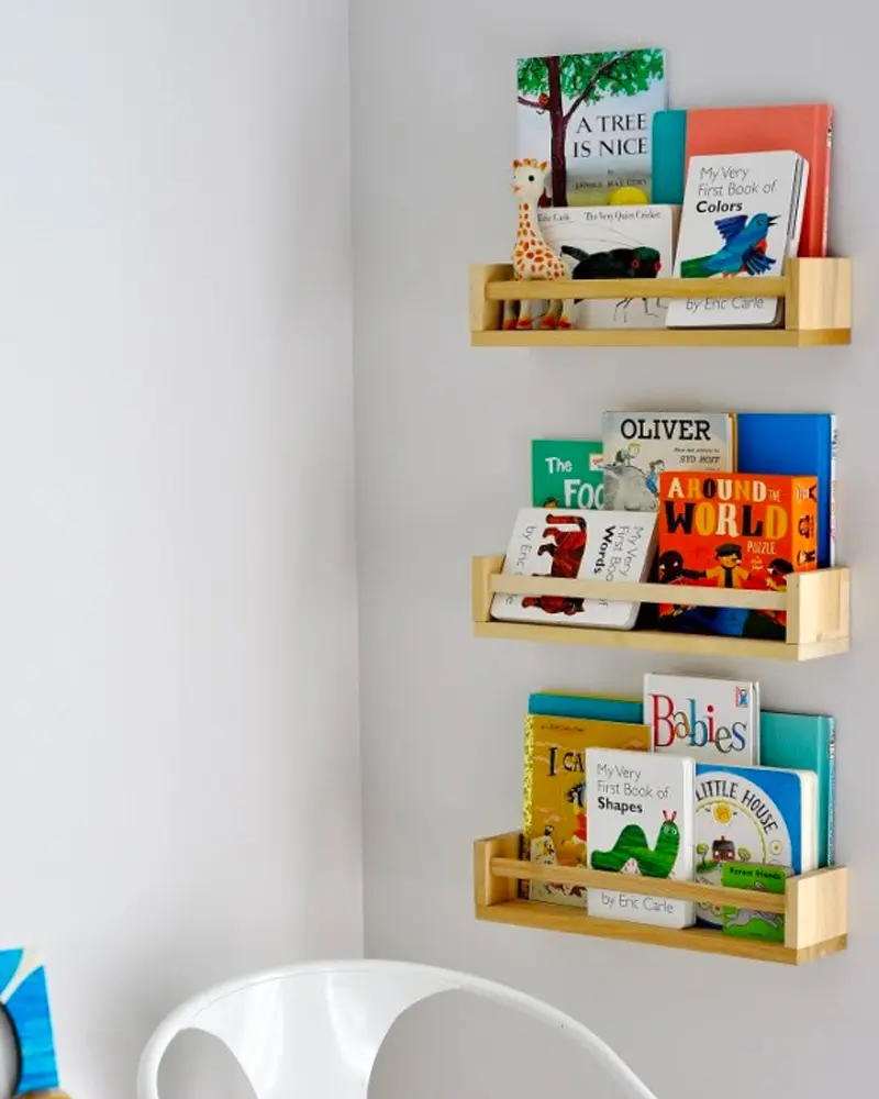 Three small wooden ledge shelves on the wall displaying children's books face-out