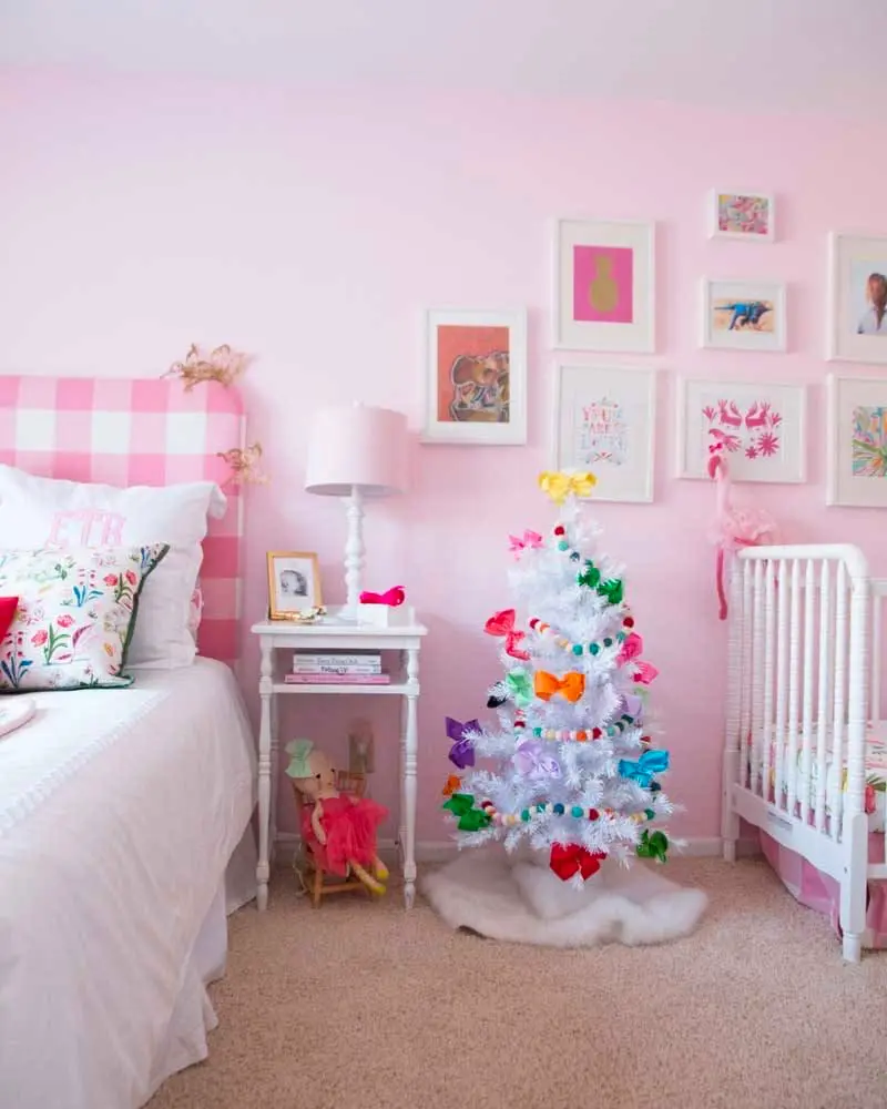 Child's bedroom with pink gingham headboard, a crib and a white Christmas tree decorated with rainbow ornaments