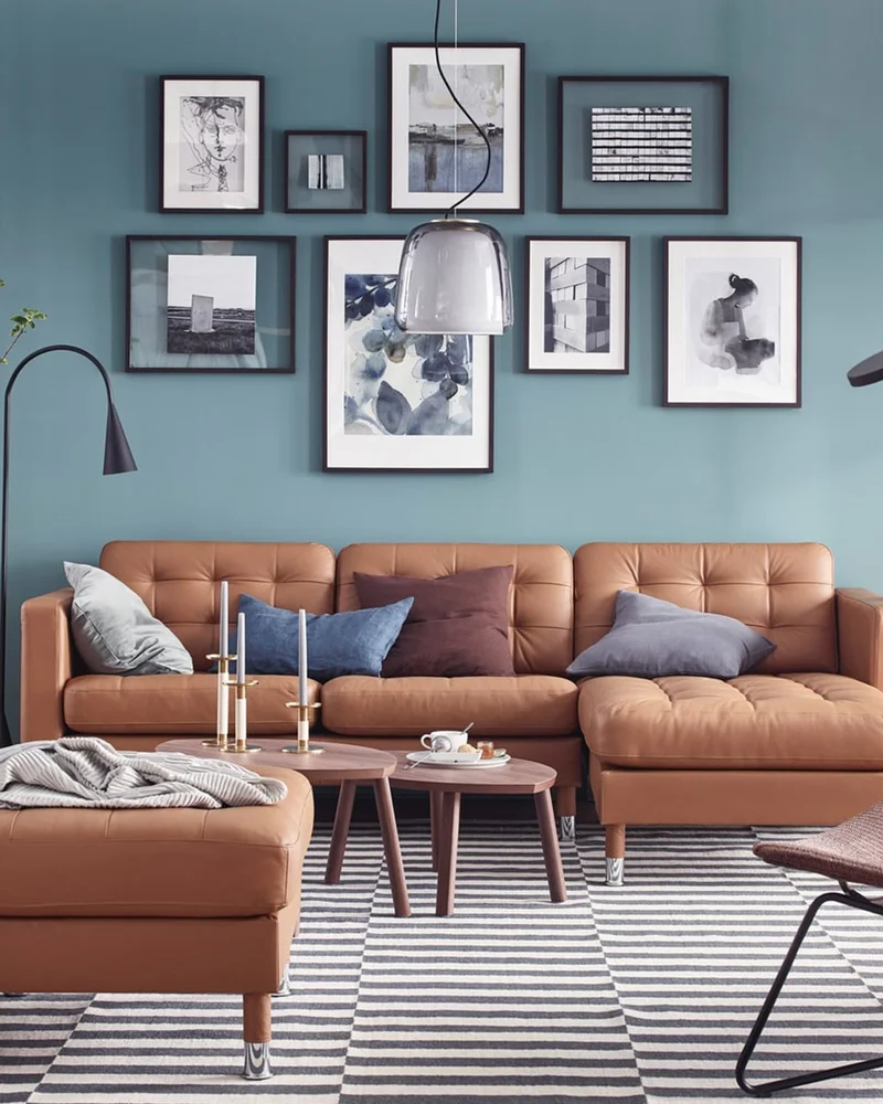 Black and white gallery wall above a tan leather sectional on a blue wall