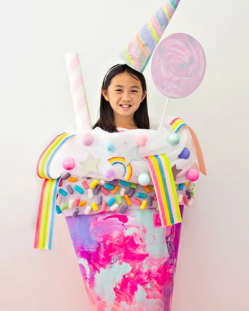 Girl inside a giant marbled pink milkshake cup with sprinkles, rainbow candy, a straw and a unicorn horn