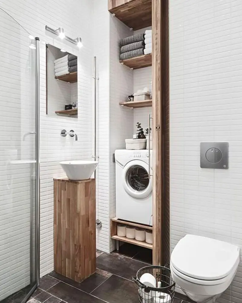 Compact bathroom with open wood shelving around a washing machine, wood sink stand and wall-hung toilet
