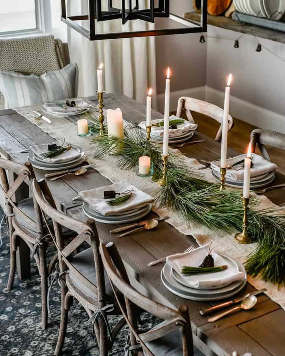 Long rustic table with a pine runner, brass candlesticks with white tapers and gray plates