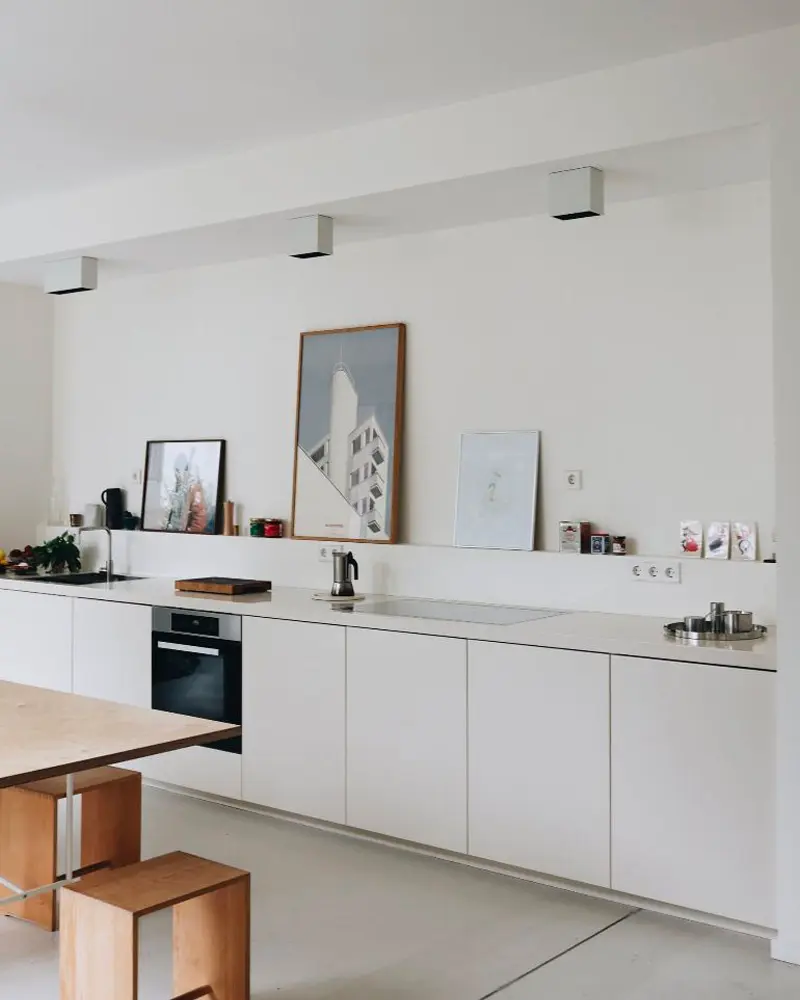 Long white kitchen run with artwork leaning on the counter and wood stools