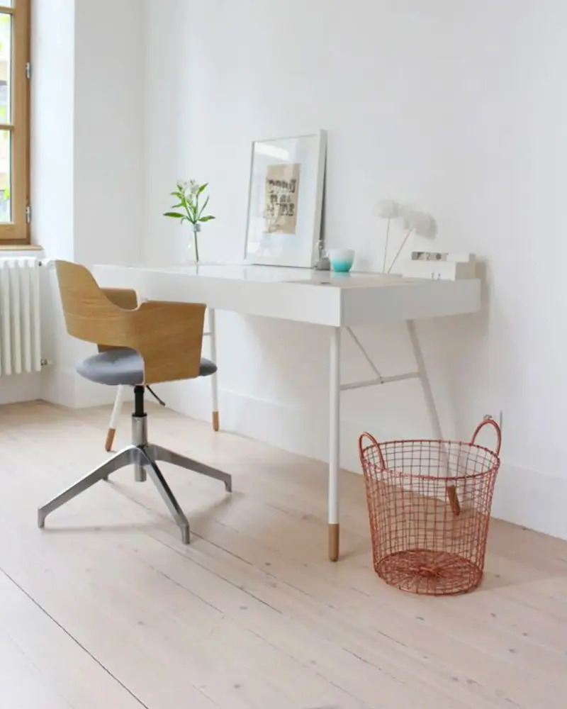 White desk with wood and gray swivel chair, copper wire basket and small framed print