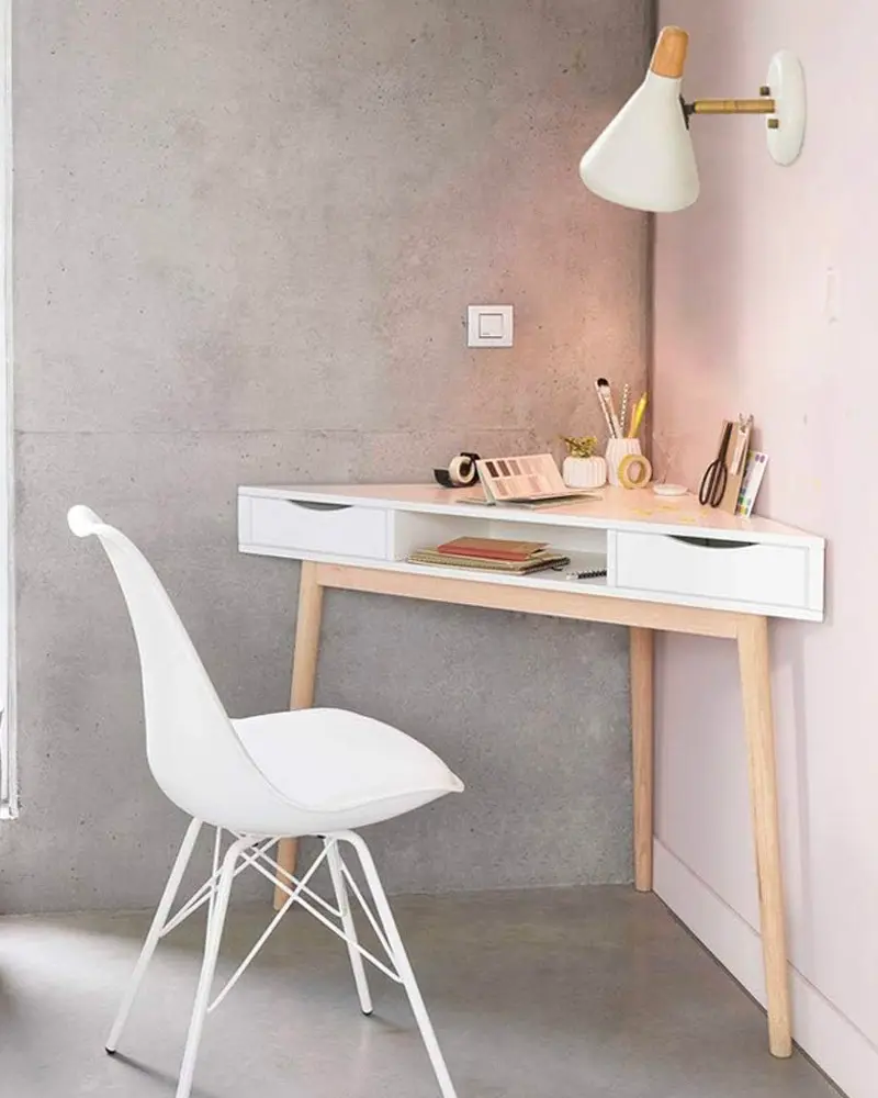 White corner desk with wood legs, white molded chair and wall-mounted lamp against a concrete-look wall