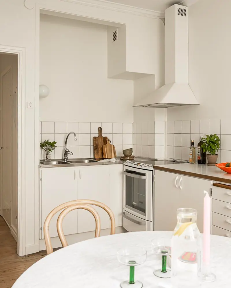 Small white kitchen with white range hood, square tile backsplash and round marble table with bentwood chair
