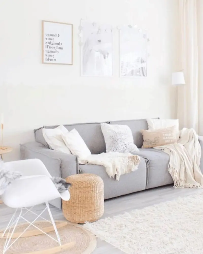 Bright living room with a light gray sofa, cream throws and pillows, a white rocking chair, a woven pouf and a shaggy rug
