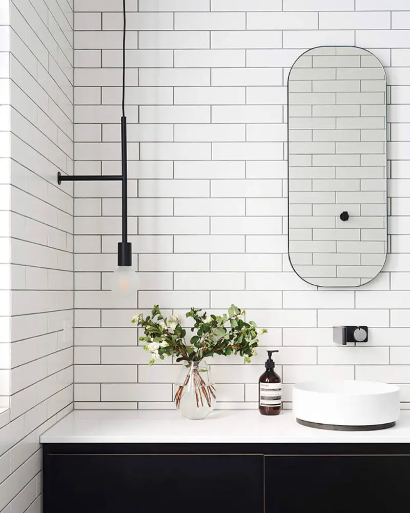 White subway tile wall with black vanity, rounded mirror, black faucet and pendant bulb
