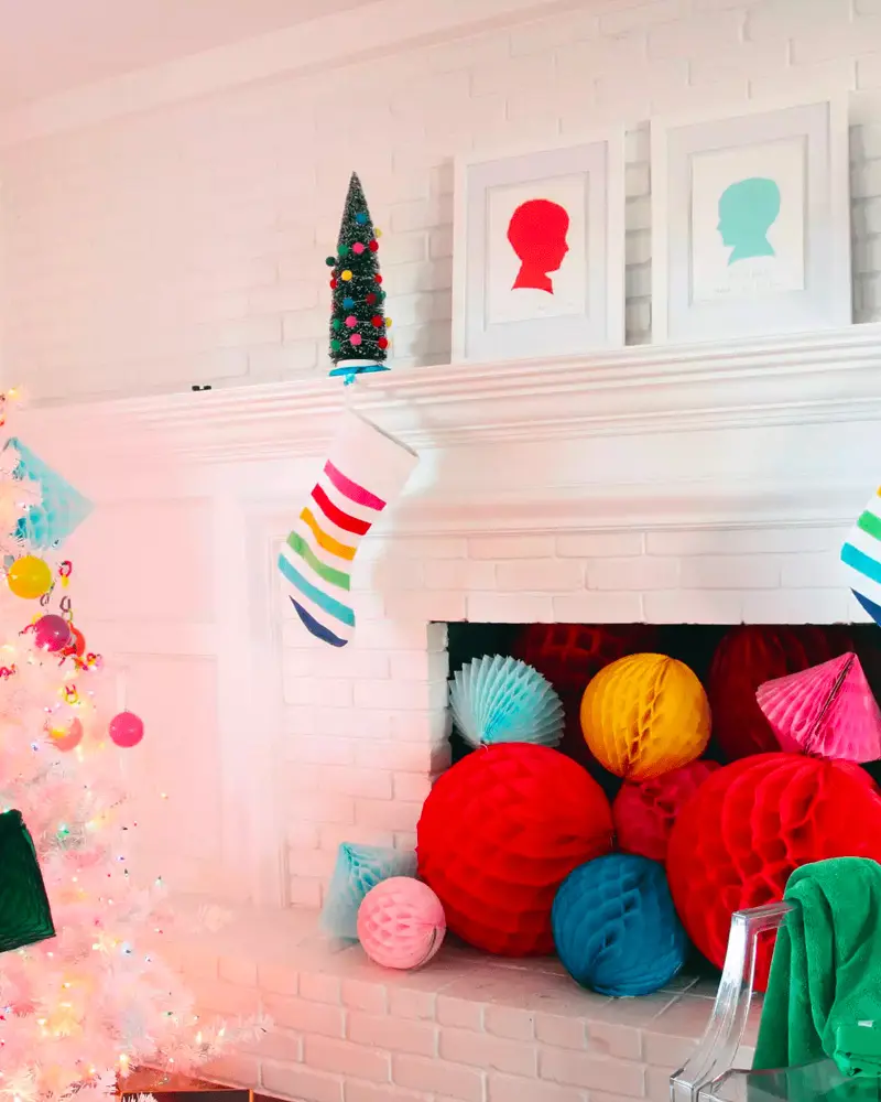 White brick fireplace filled with colorful honeycomb paper balls, a rainbow stocking and silhouette prints