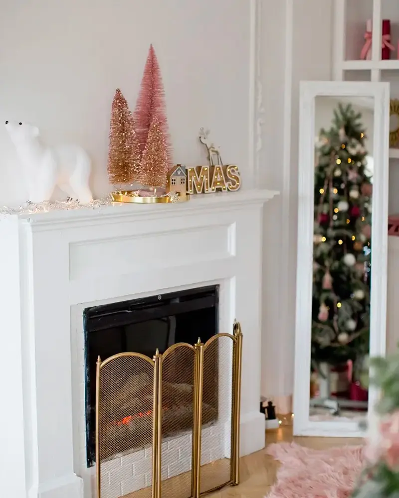 White mantel with pink and gold bottle brush trees, a polar bear, XMAS letters and a brass fire screen