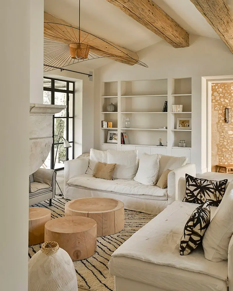 Beige sofas, tree-stump side tables and built-in white shelves under pale wood beams