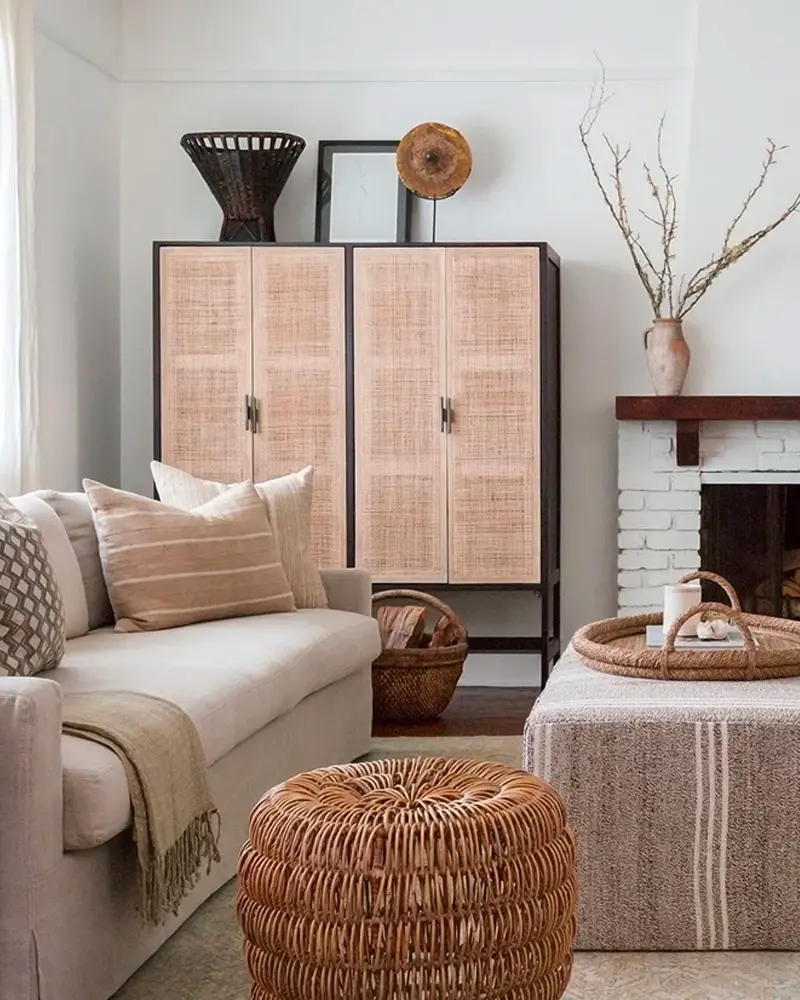 Cane-front cabinet, a rattan pouf, a striped ottoman and a white brick fireplace