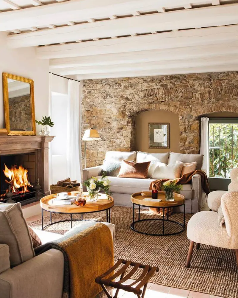 Exposed stone wall, a lit fireplace, round wood coffee tables and cream sofas