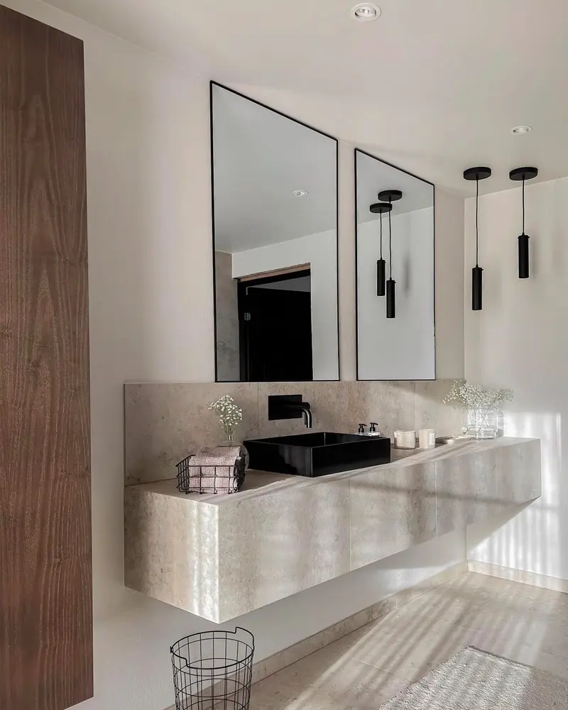 Floating pale stone vanity with black vessel sink, two black-framed mirrors and black pendant lights