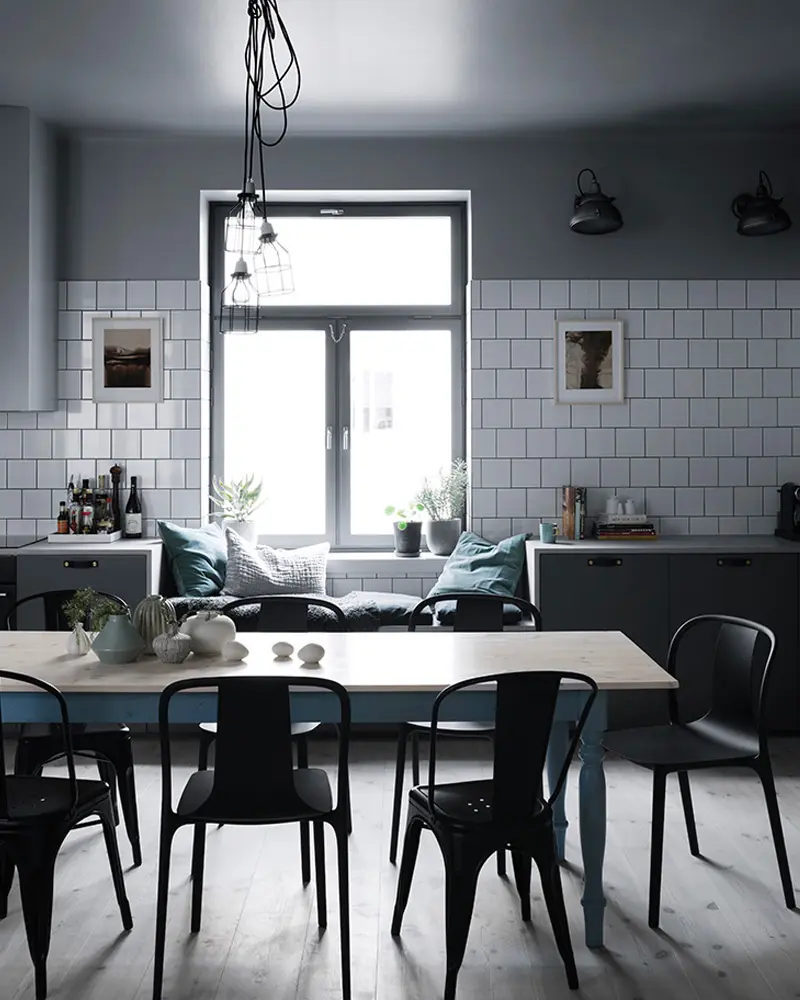 Gray walls and white subway tile with a pale table, black metal chairs and a cage pendant
