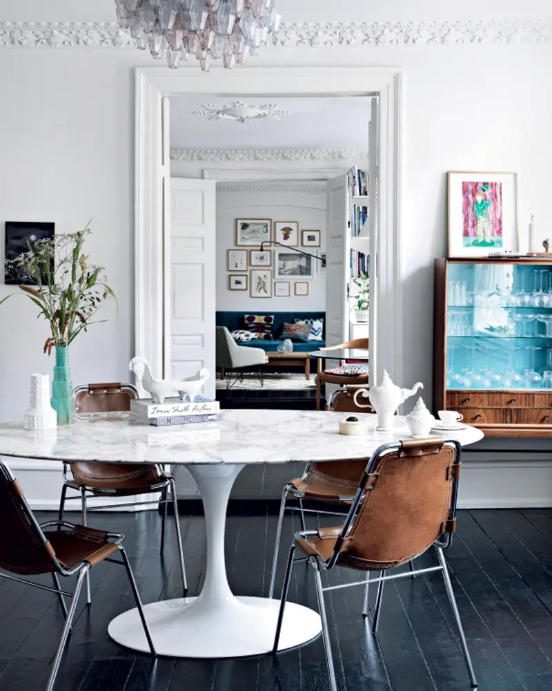 White marble tulip table with leather sling chairs under a crystal chandelier